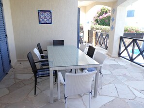 A glass-top table with wicker chairs, a tiled wall, and a stone floor.