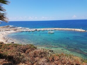 Eine Küstenlandschaft mit Booten an einem Steg, klarem blauen Wasser und felsigem Ufer.
