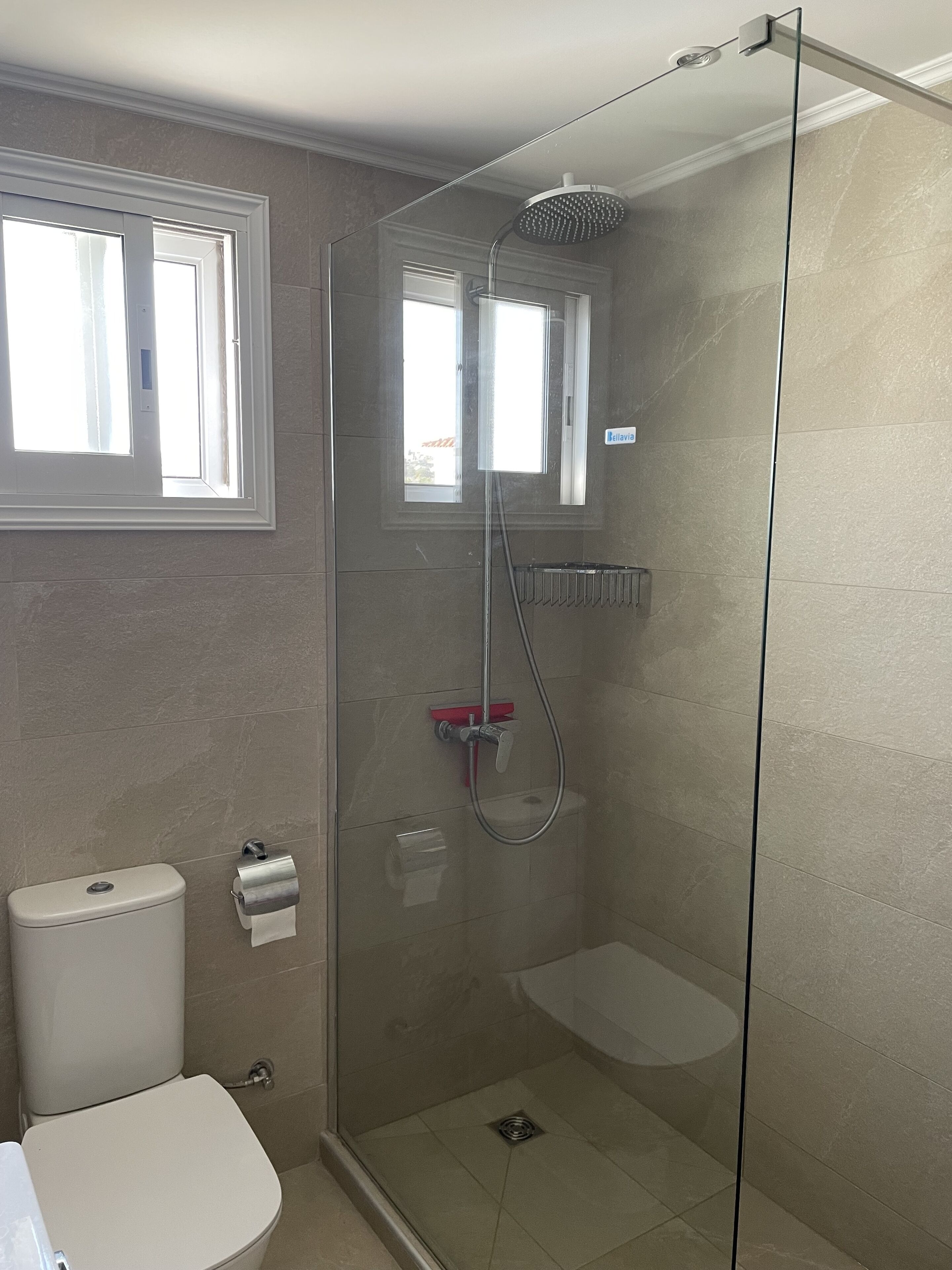 A modern bathroom with a glass-enclosed shower, a toilet, and a window.