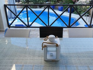 A glass table with a white decorative object, a wicker chair, and a view of a swimming pool through a metal railing.