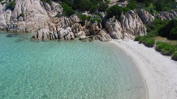 Una playa con agua turquesa cristalina, arena blanca y formaciones rocosas.