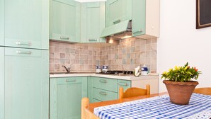 Una cocina con gabinetes color turquesa, un salpicadero de azulejos, una estufa y una mesa de comedor con mantel a cuadros.