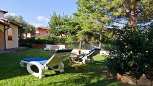 Un jardín con sillas de jardín y una mesa, rodeado de follaje y un muro de piedra.