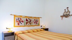 Un dormitorio con colcha a rayas, un adorno de pared con diseños de mariposas y una mesita de noche de madera con lámpara.