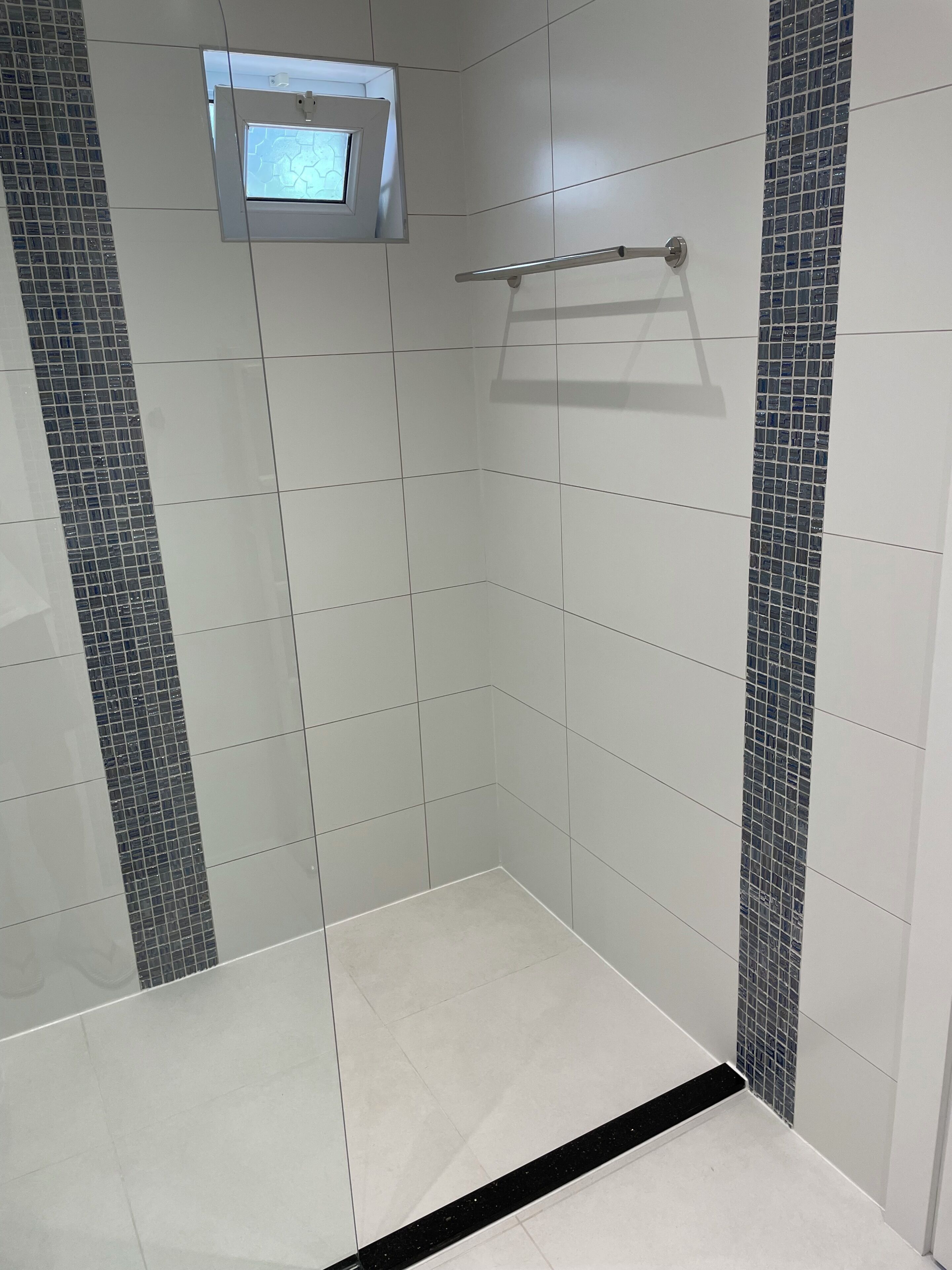 Een badkamer met witte tegels, een klein raam en een handdoekrek.