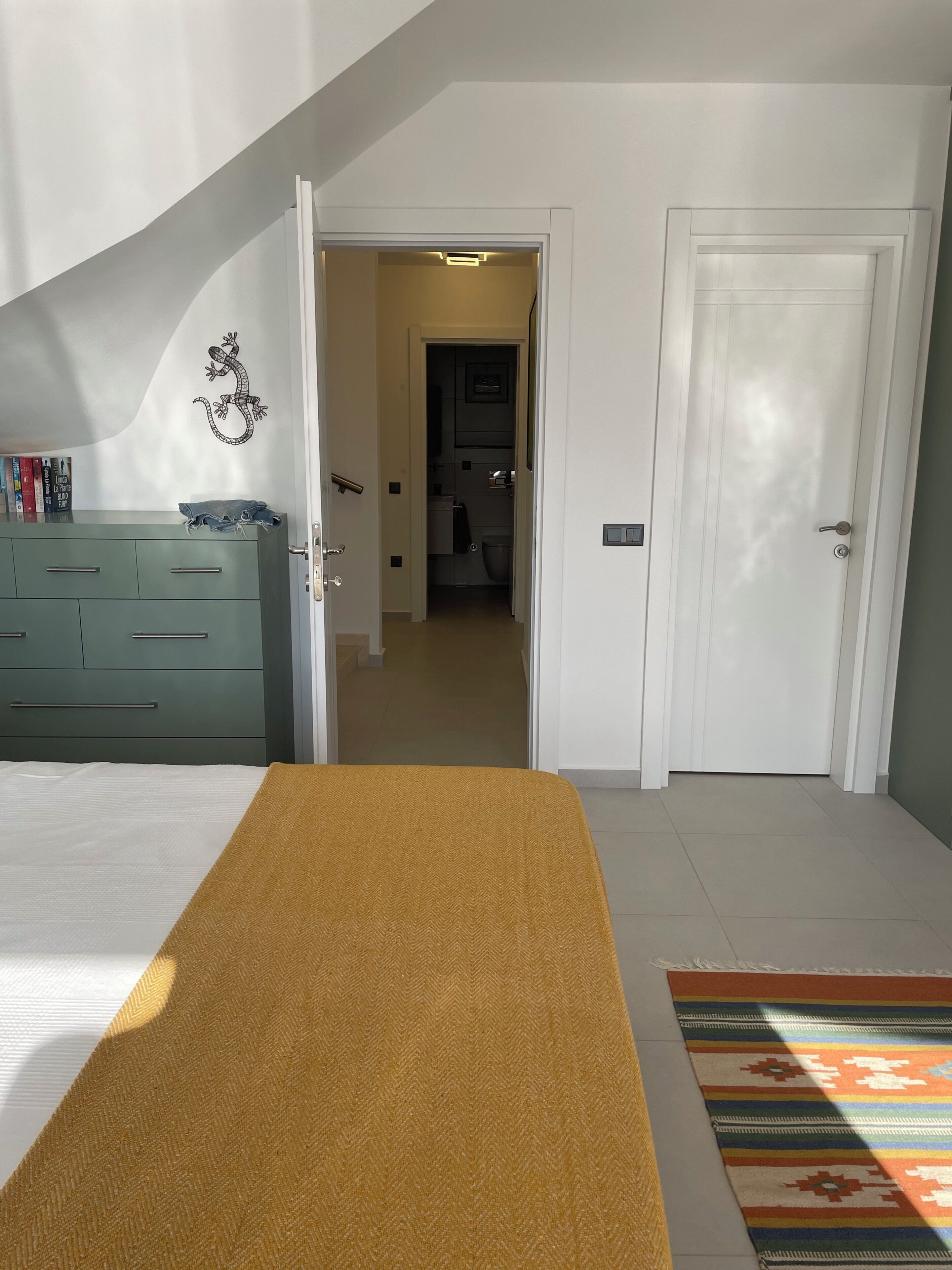 Un dormitorio con cama, cómoda, pasillo que lleva a un baño y una puerta.