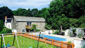 A backyard with a swimming pool, a wooden swing set, and a stone house.