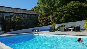 A swimming pool with clear blue water, surrounded by stone walls and a wooden deck.