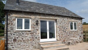 A stone house with a tiled roof, white-framed windows, and a glass door.