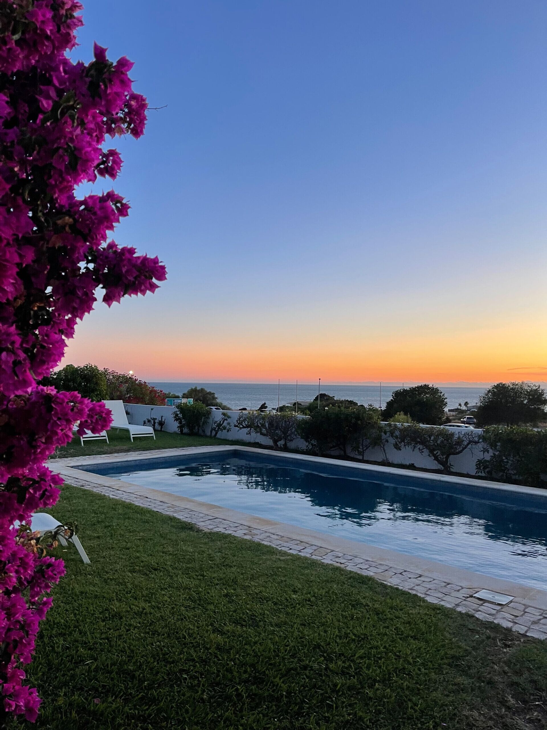 A swimming pool with a view of the ocean at sunset.