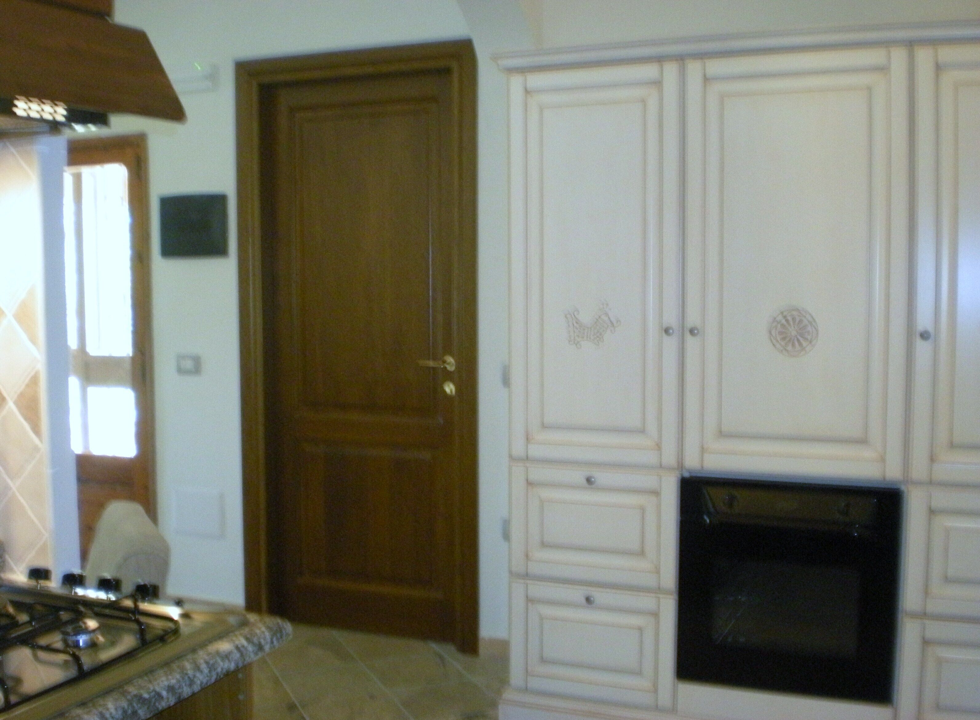 Une cuisine équipée d’une cuisinière à gaz, d’une porte en bois et de meubles blancs ornés de motifs décoratifs.