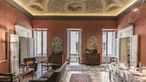 A spacious room with a large sofa, a dining table set for a meal, and a view of the outside through a doorway. - The Rediscovered House (Firenze)