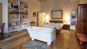 A spacious room with a large white bathtub, a wooden floor, a bookshelf filled with books, and a ceiling with intricate designs. - The Rediscovered House (Firenze)