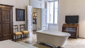 A room with a bathtub, wooden furniture, a television, and a painting on the wall. - The Rediscovered House (Firenze)