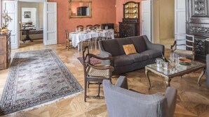 A spacious room with a high ceiling featuring ornate plasterwork and frescoes, a dining area with a long table set for six, and a seating area with a sofa and armchairs. - The Rediscovered House (Firenze)