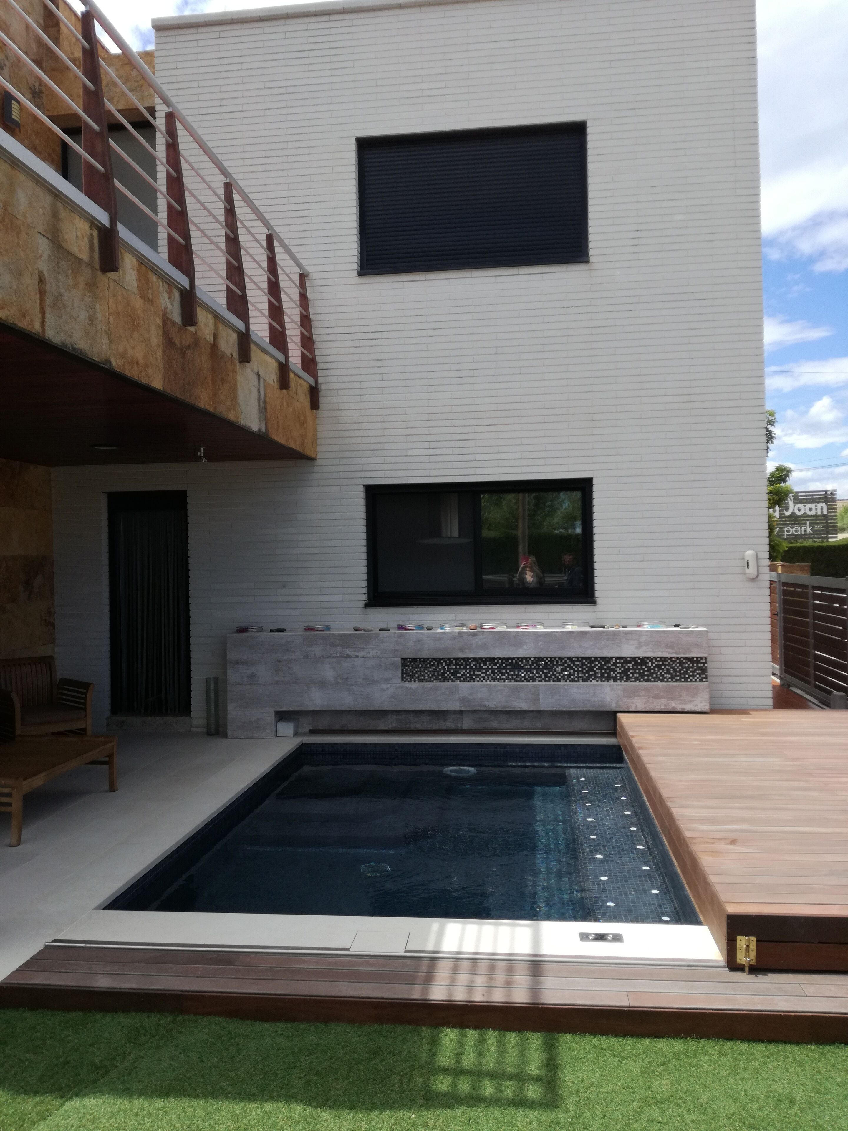 A modern building with a pool, a wooden deck, and a seating area with a bench and table.