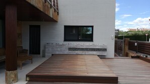 Un patio exterior moderno con terraza de madera, banca integrada y pared blanca con ventana.