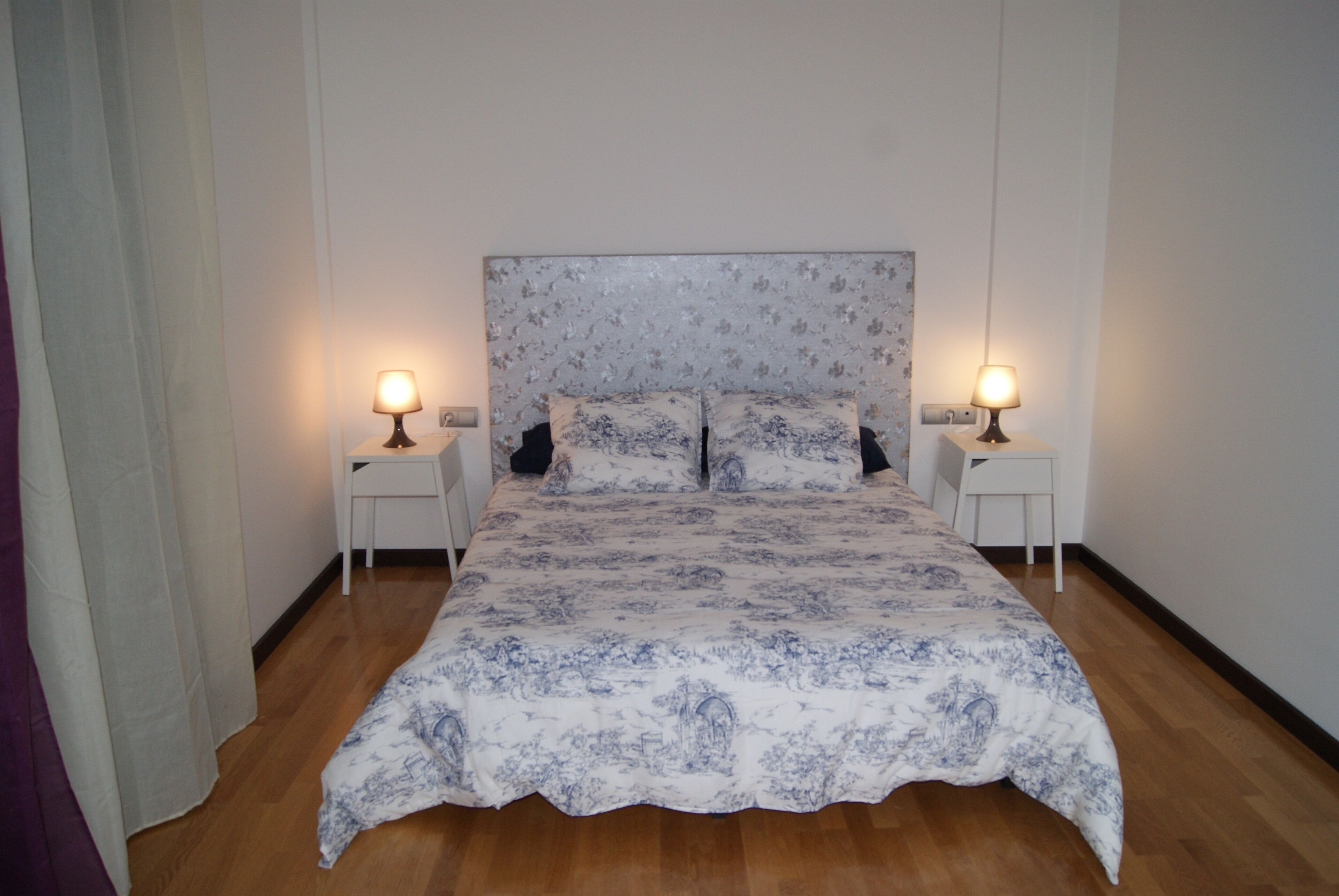 Une chambre à coucher avec une couvre-lit à motifs floraux, deux tables de chevet avec des lampes et un plancher en bois.