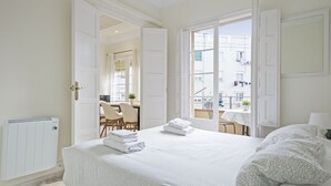 Hotellihuone, jossa on suuri sänky, patteri, ruokailutila tuoleineen ja näkymä ulkona oleviin rakennuksiin.