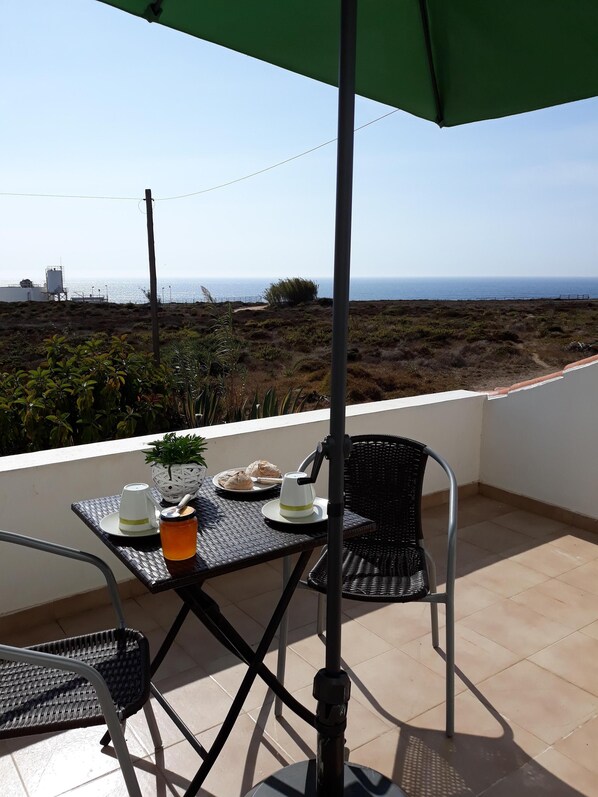 A balcony with a table set for two, a chair, and a view of the sea.