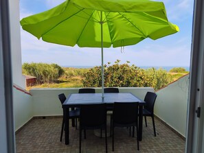 A balcony with a table and chairs, a green umbrella, and a view of the sea.