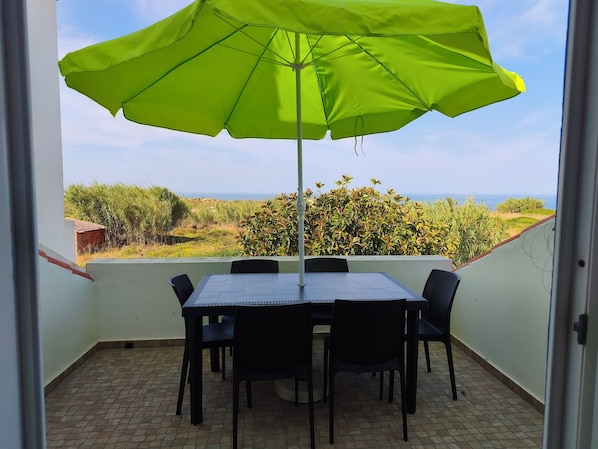 A balcony with a table and chairs, a green umbrella, and a view of the sea.