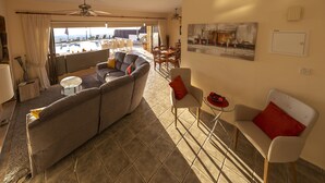 A spacious living area with a sofa, chairs, and a dining table. A balcony with a view is visible through the glass doors. - Villa Callista -  Modern Villa that sleeps 8 guests  in 4 bedrooms (Paphos)