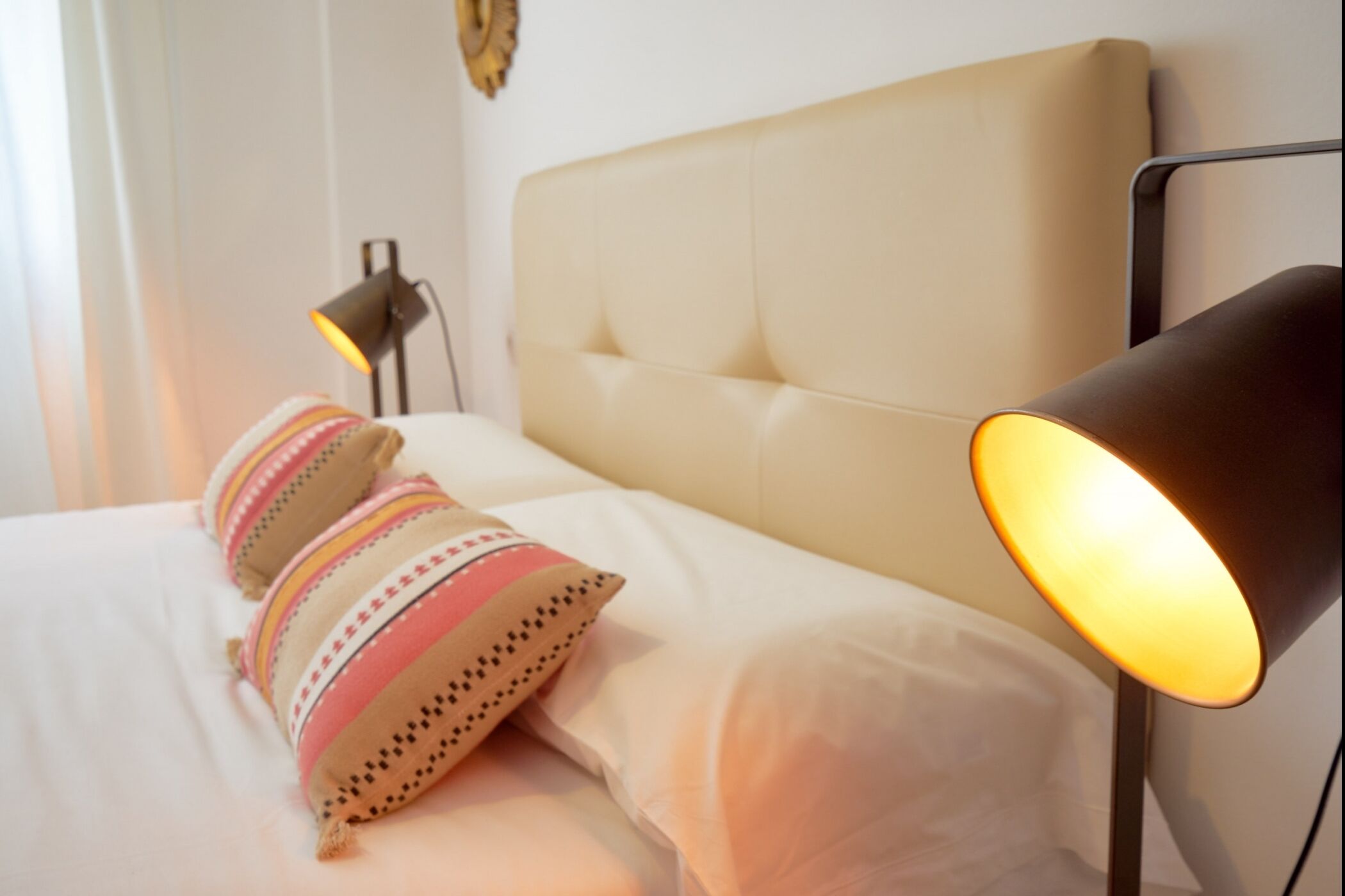 A neatly made bed with a headboard, two decorative pillows, and a bedside lamp.