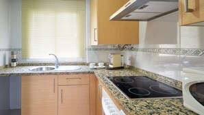A kitchen with wooden cabinets, a stainless steel sink, a built-in stove, and a window with blinds. - iloftmalaga Puerta del Mar II (Málaga)