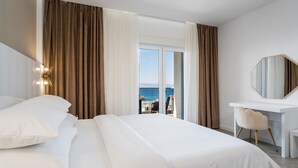 A hotel room with a large bed, a desk, and a view of the sea through the window.