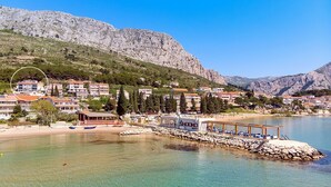 A coastal town with buildings, a beach, and a rocky mountain backdrop.