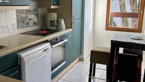 A compact kitchen with teal cabinets, a dishwasher, an oven, and a dining area with a table and chair.