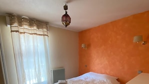 A bedroom with a bed, a radiator, a window with curtains, and a wall-mounted lamp.