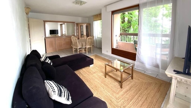 A living room with a sofa, a coffee table, and a TV. There is a kitchen area with cabinets and a dining table. - Waterfront apartment in the historic district with a large terrace. (Annecy)