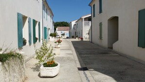 Una stretta via con edifici bianchi, persiane verdi e piante in vaso.