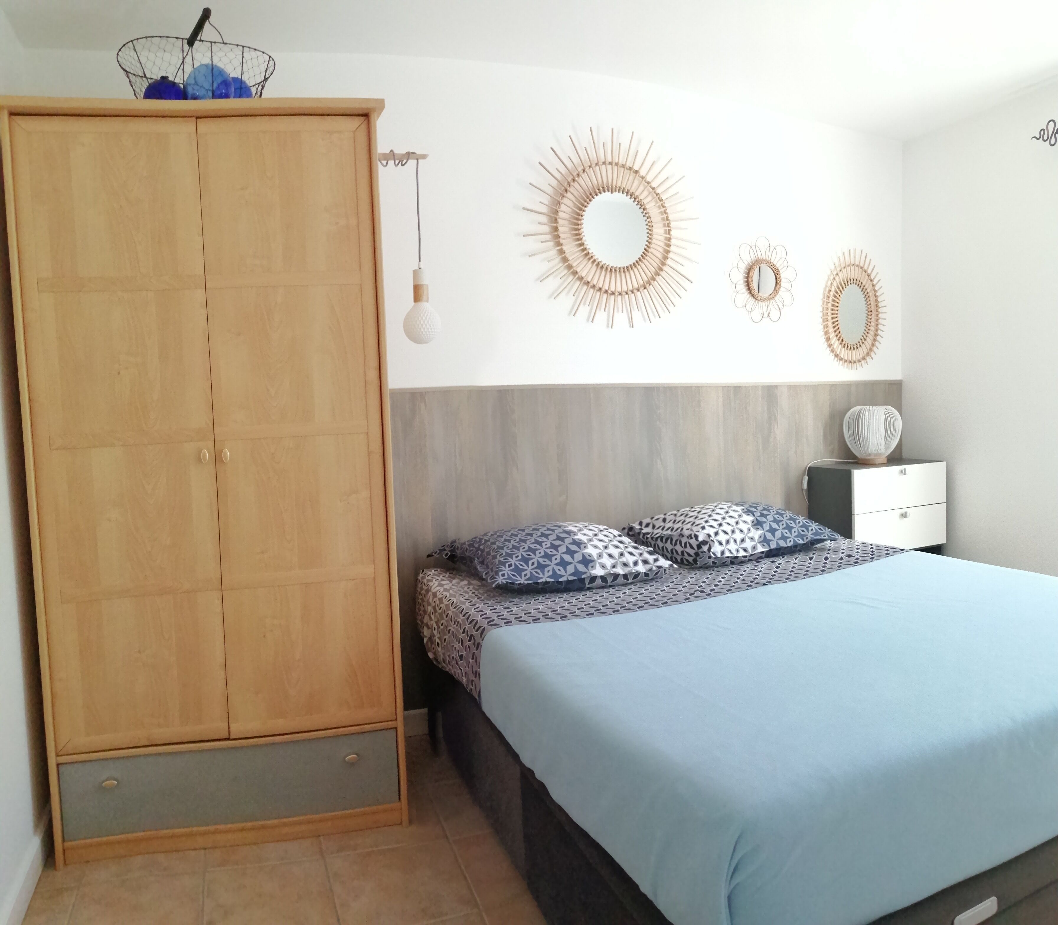 Ein Schlafzimmer mit einem Holzschrank, einem Bett mit gemusterten Betttextilien und dekorativen Wandspiegeln.
