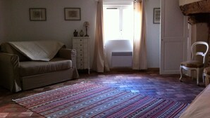 Ein gemütliches Zimmer mit einer Couch, einem kleinen Tisch mit Lampe, einem Sessel und einem gemusterten Teppich.