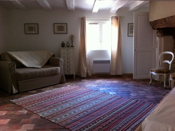 Ein gemütliches Zimmer mit einer Couch, einem kleinen Tisch mit Lampe, einem Sessel und einem gemusterten Teppich.