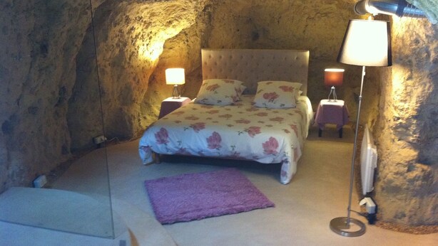Ein Schlafzimmer mit Steinwand, einem Bett mit floralem Bettzeug, zwei Nachttischen mit Lampen und einem violetten Teppich.