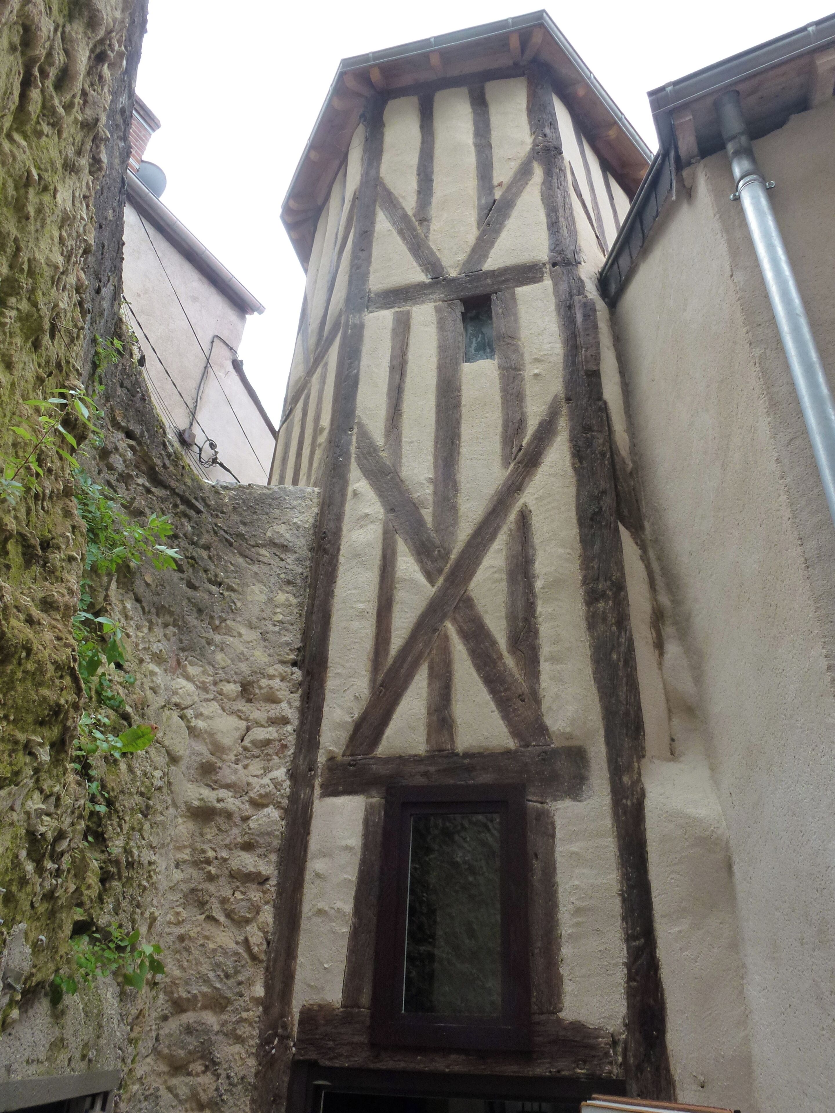 Une ruelle étroite bordée d’un bâtiment dont la charpente en bois est apparente et d’un mur en pierre.