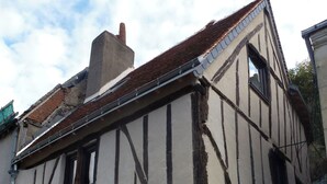 Ein traditionelles Fachwerkhäuschen mit steilem Satteldach, einem markanten Schornstein und einer kleinen Haustür.