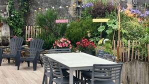 A patio with a table and chairs, surrounded by a variety of plants and flowers.
