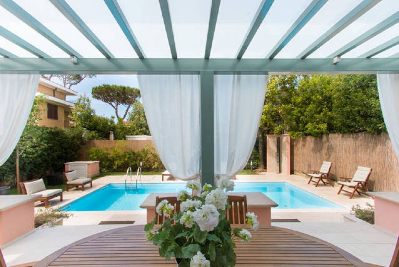An outdoor pool area with a pergola, white curtains, and lounge chairs.
