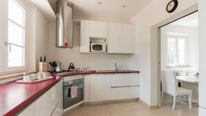 A compact kitchen with white cabinets, a stainless steel range hood, a microwave, and a red countertop. - Villa Il Rifugio, villa with private pool (Pietrasanta)