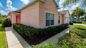 A pink house with a red door, surrounded by well-maintained hedges and a clear sky. - Town Center Reserve - Superior Disney Villa with Lake View, free WiFI & Netflix (Davenport)
