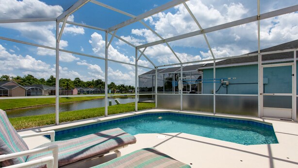 An outdoor swimming pool with lounge chairs, a covered area, and a view of a water body and houses in the background. - Town Center Reserve - Superior Disney Villa with Lake View, free WiFI & Netflix (Davenport)