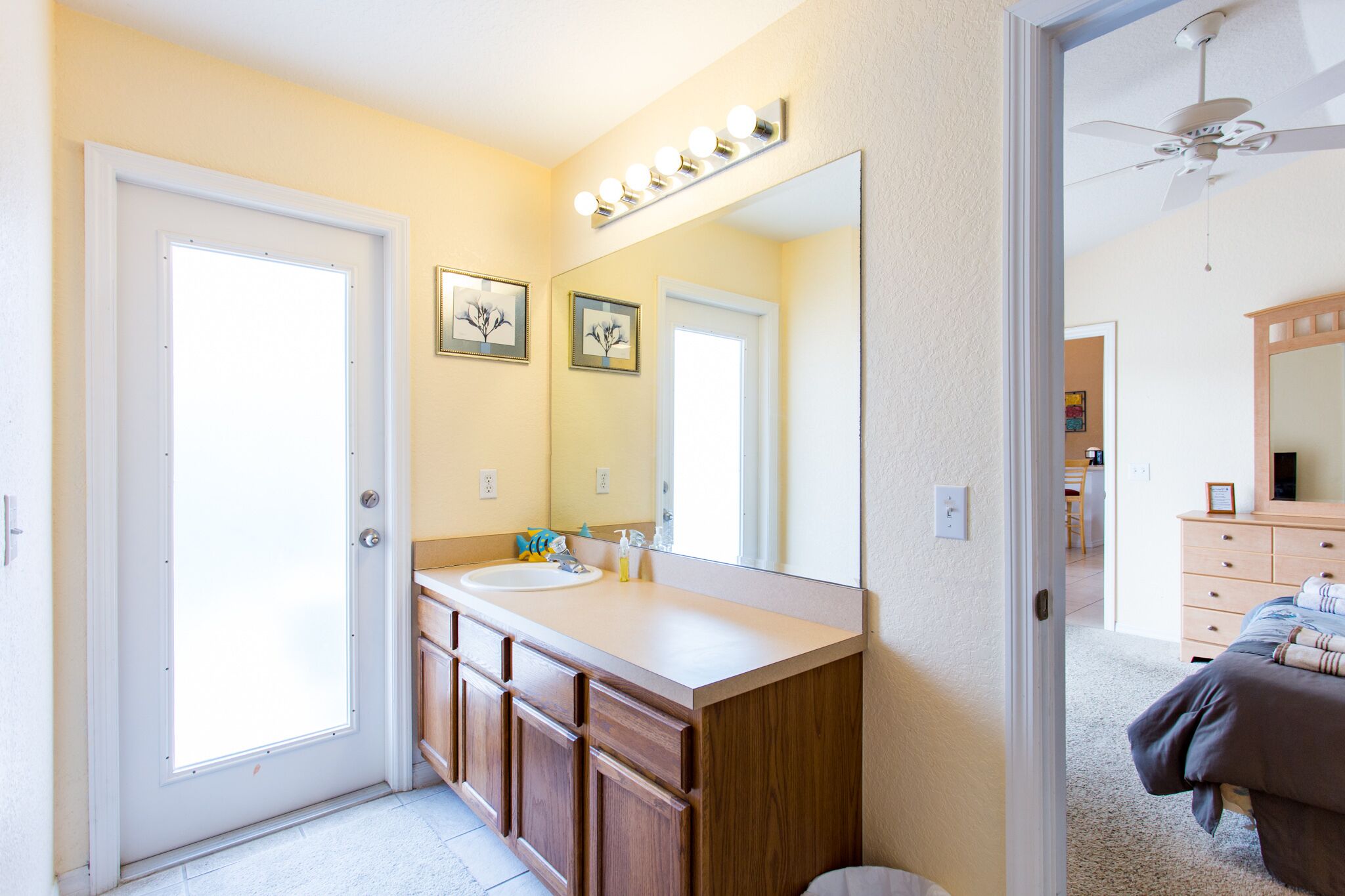 A bathroom with a large mirror, vanity, and a door leading to another room.