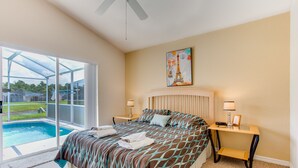 A bedroom with a large bed, a painting of the Eiffel Tower, a nightstand, a lamp, and a view of a swimming pool. - Town Center Reserve - Superior Disney Villa with Lake View, free WiFI & Netflix (Davenport)