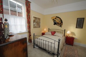 Un dormitorio con cama, mesitas de noche, ventana con cortinas y decoración en la pared.