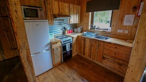 Cocina de cabaña de madera con refrigerador, microondas, estufa, lavabo y armarios de madera.